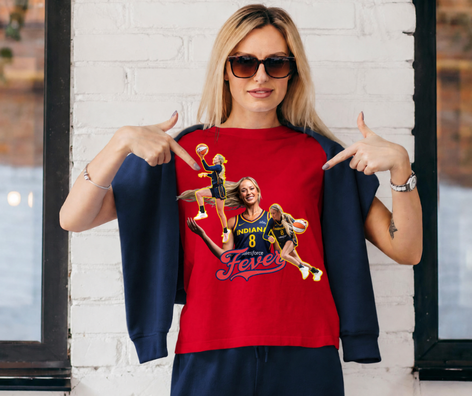A woman wearing a red crewneck sweatshirt with a custom basketball player graphic, styled with a navy blue cardigan and sunglasses, posing in front of a white brick wall.